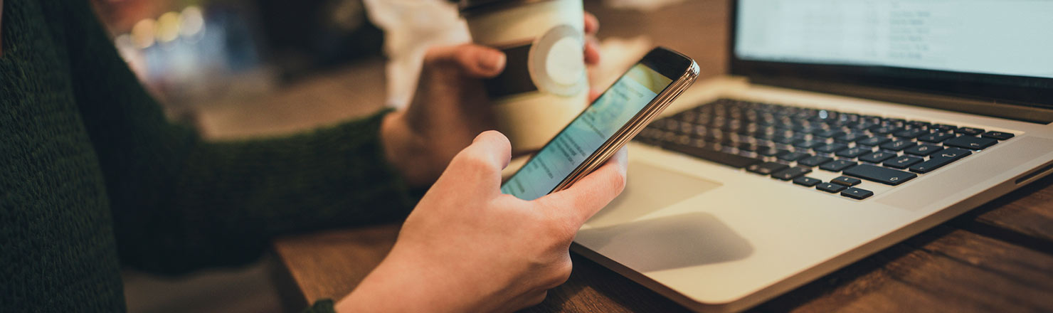 Woman holding phone, coffee at laptop