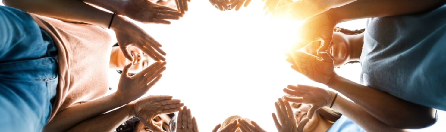 A group of friends in a circle smiling while forming a heart with their hands. 